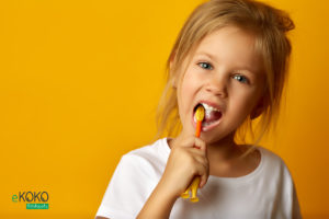 dziewczynka w białej koszulce czyści zęby na żółtym tle - fototapeta do gabinetu stomatologicznego