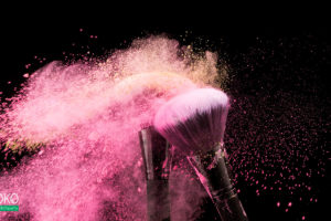 pędzle kosmetyczne i chmura pudru w różowych tonach - fototapeta do salonu kosmetycznego
