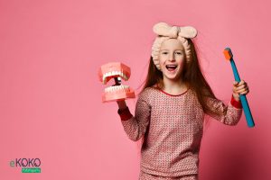 uśmiechnięta dziewczynka ze szczoteczką i modelem uzębienia na różowym tle - fototapeta do gabinetu stomatologicznego