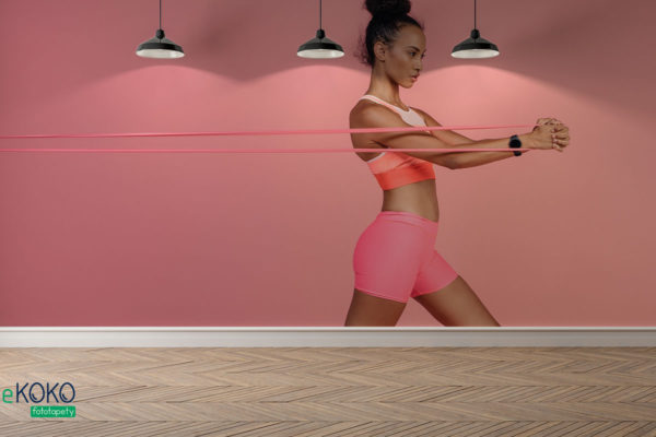 wysportowana kobieta w różowym stroju wykonuje ćwiczenia z gumową taśmą - fototapeta do siłowni, klubu fitness