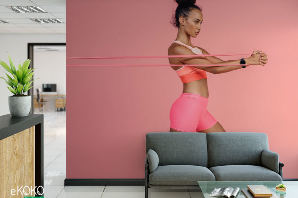 wysportowana kobieta w różowym stroju wykonuje ćwiczenia z gumową taśmą - fototapeta do siłowni, klubu fitness
