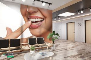 kobieta wskazuje palcem swoje białe zęby na jasnym tle - fototapeta do gabinetu stomatologicznego