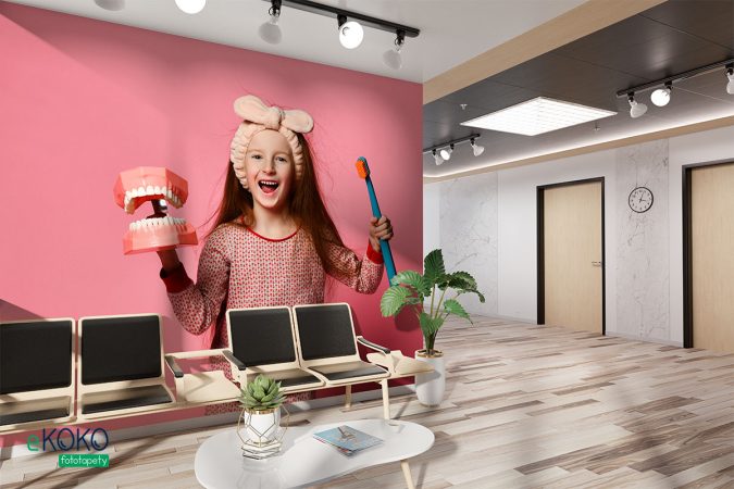 uśmiechnięta dziewczynka ze szczoteczką i modelem uzębienia na różowym tle - fototapeta do gabinetu stomatologicznego